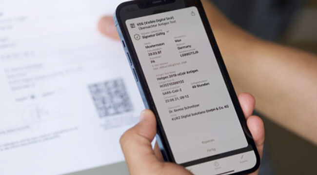 El Sello Digital Visible (VDS) protege los documentos en papel o digitales contra el uso indebido y la falsificación. Imagen de manos que sostienen un smartphone y escanean el código QR seguro en un documento de papel
