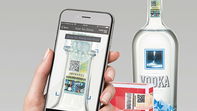 Modular physical and digital solutions for tax stamps and brand protection Image of a hand holding a mobile phone and scanning the QR code on a secure label on a bottle of alcohol.